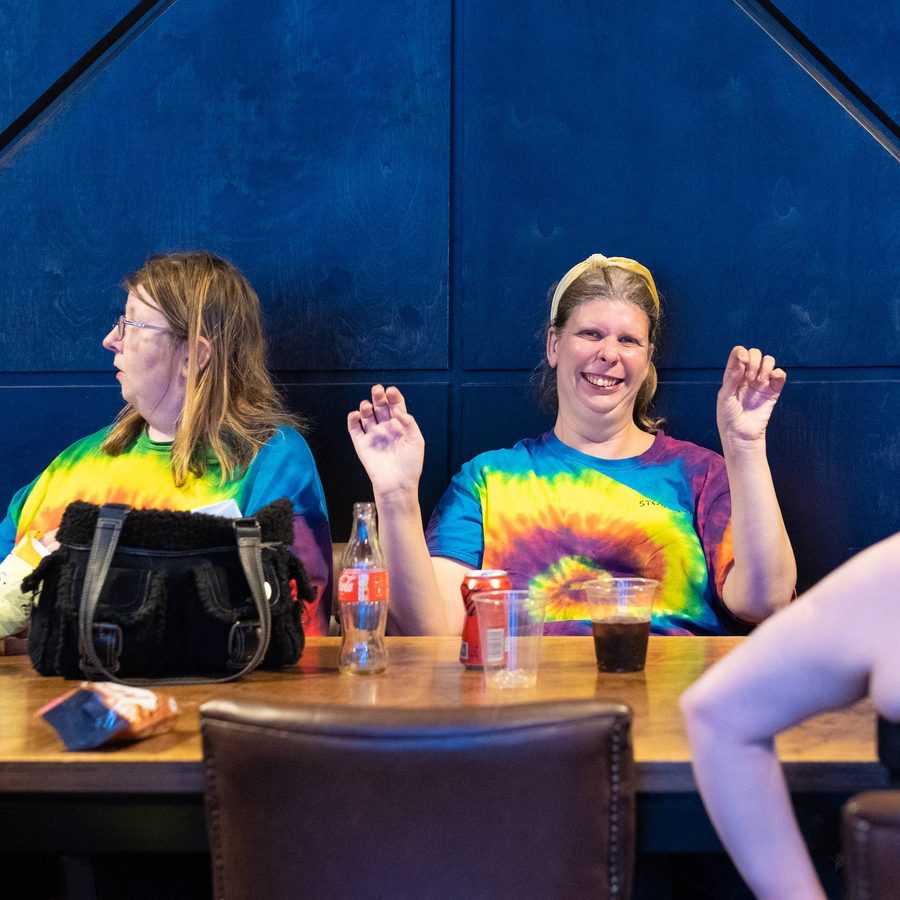 Two women sat at a table wearing tie-dye Kaleidoscope t-shirts.